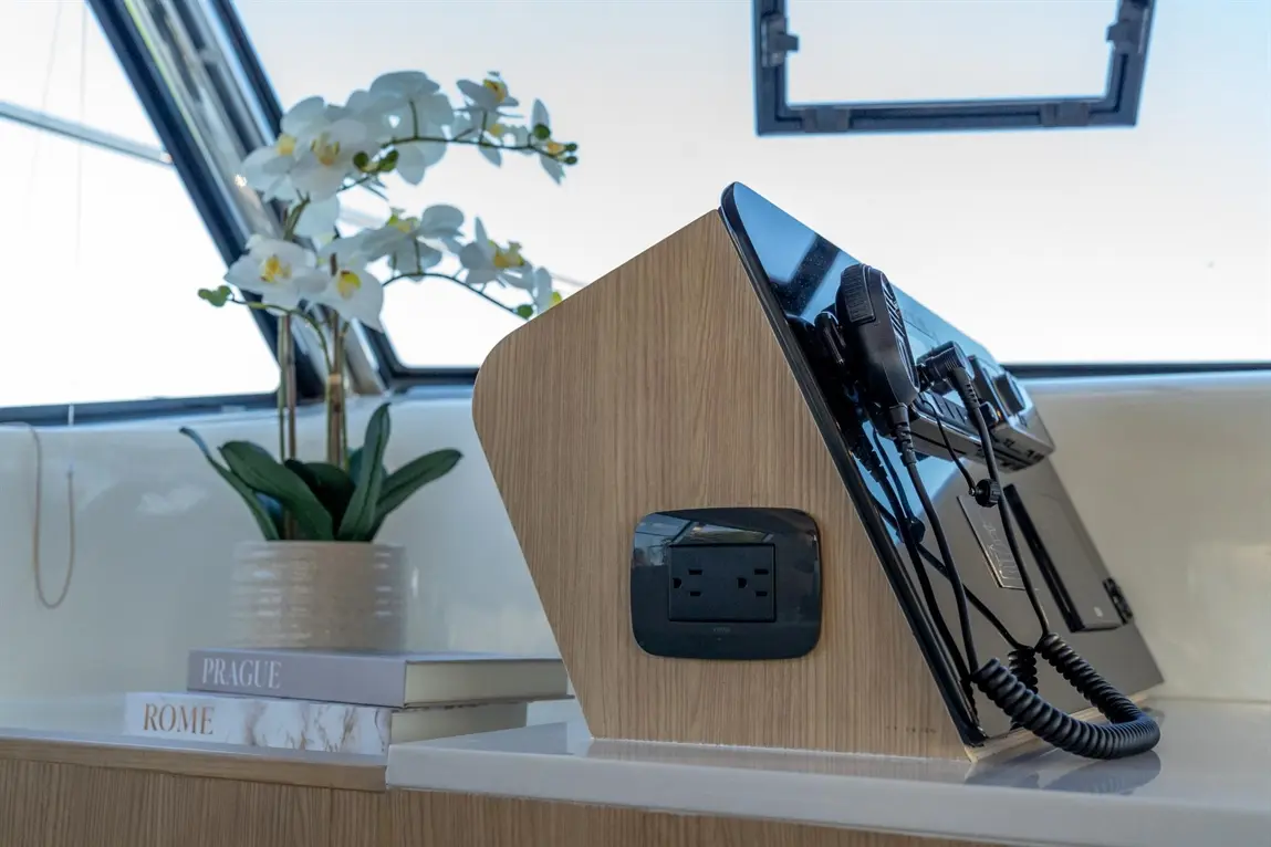 Stylish boat interior featuring a communication device, power socket, and a vase with orchids beside stacked books.